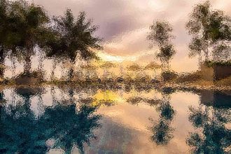 Sunset over a calm lake with tree silhouettes reflected in rippled water.