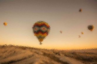 Colorful hot air balloons floating above a sandy landscape at sunset, with a warm gradient sky.