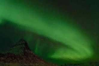 Aurora borealis glowing bright green over a rocky landscape at night.
