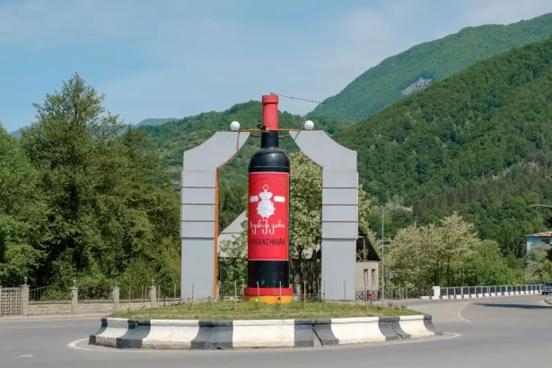 Giant wine bottle sculpture in the center of a roundabout, with green hills and trees in the background.