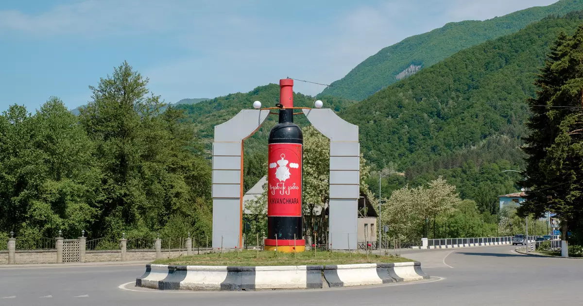 Giant wine bottle sculpture in the center of a roundabout, with green hills and trees in the background.