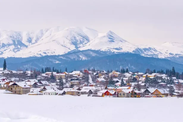 Snow-covered town in a valley with towering mountains in the background.