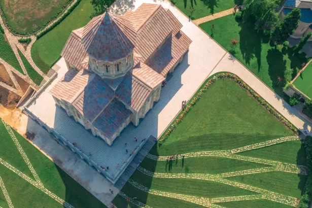 Aerial view of a stone church with a copper roof, surrounded by manicured lawns, flower beds, and intersecting stone pathways.