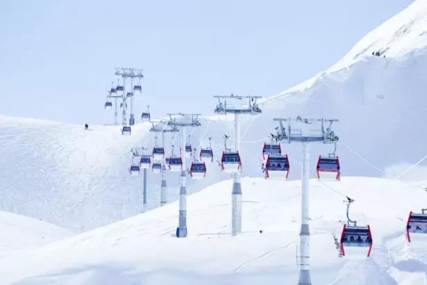 Chairlift over a snow-covered mountain with red gondolas and blue sky.