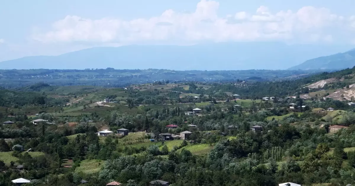 Expansive rural valley with scattered houses, green fields, and distant mountains under a blue sky with clouds.