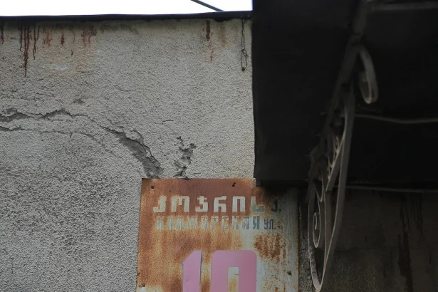 Old Russian-era sign beside a modern Georgian-English sign shows Tbilisi's shift from Russian to English.