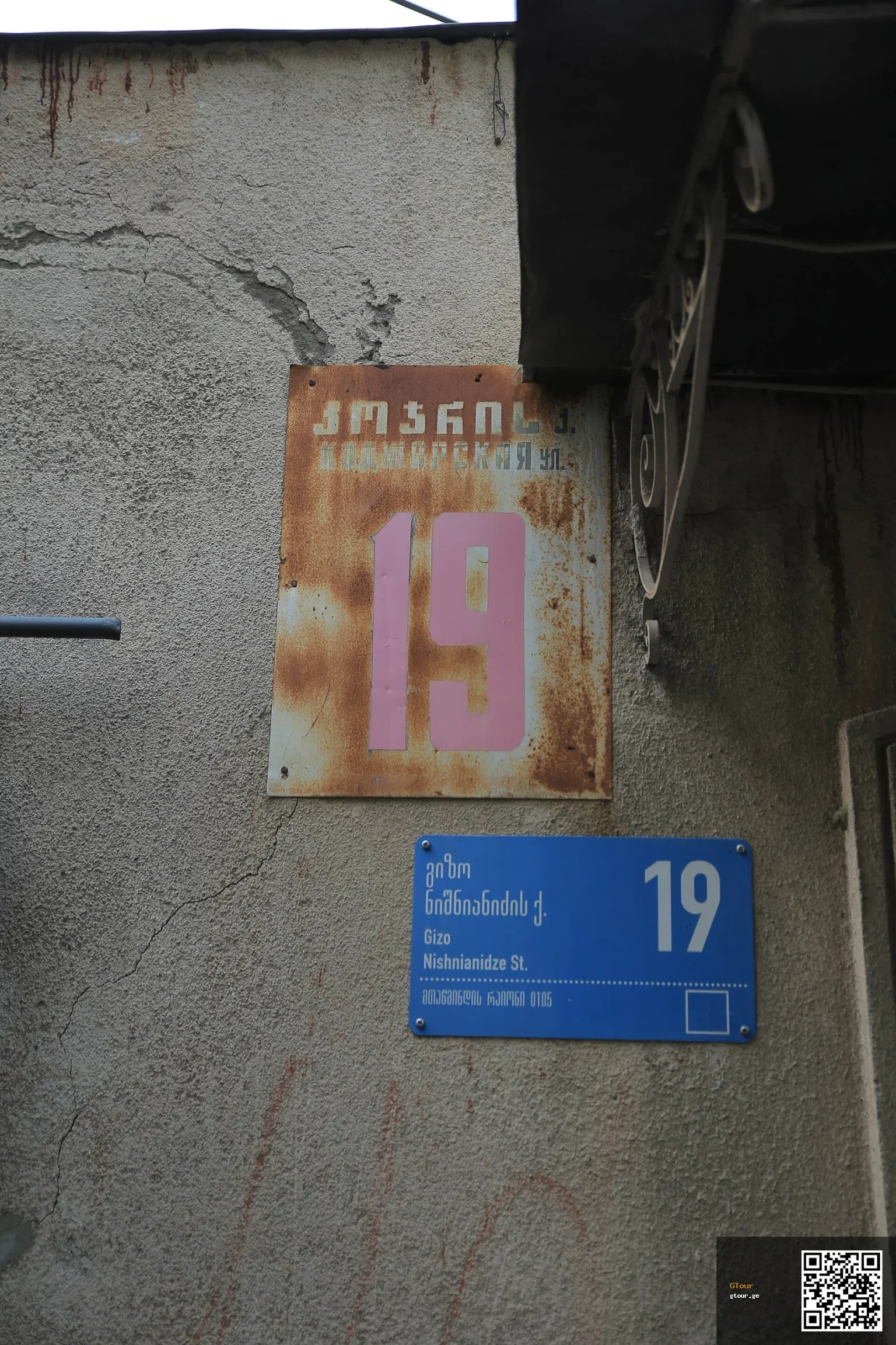 Old Russian-era sign beside a modern Georgian-English sign shows Tbilisi's shift from Russian to English.