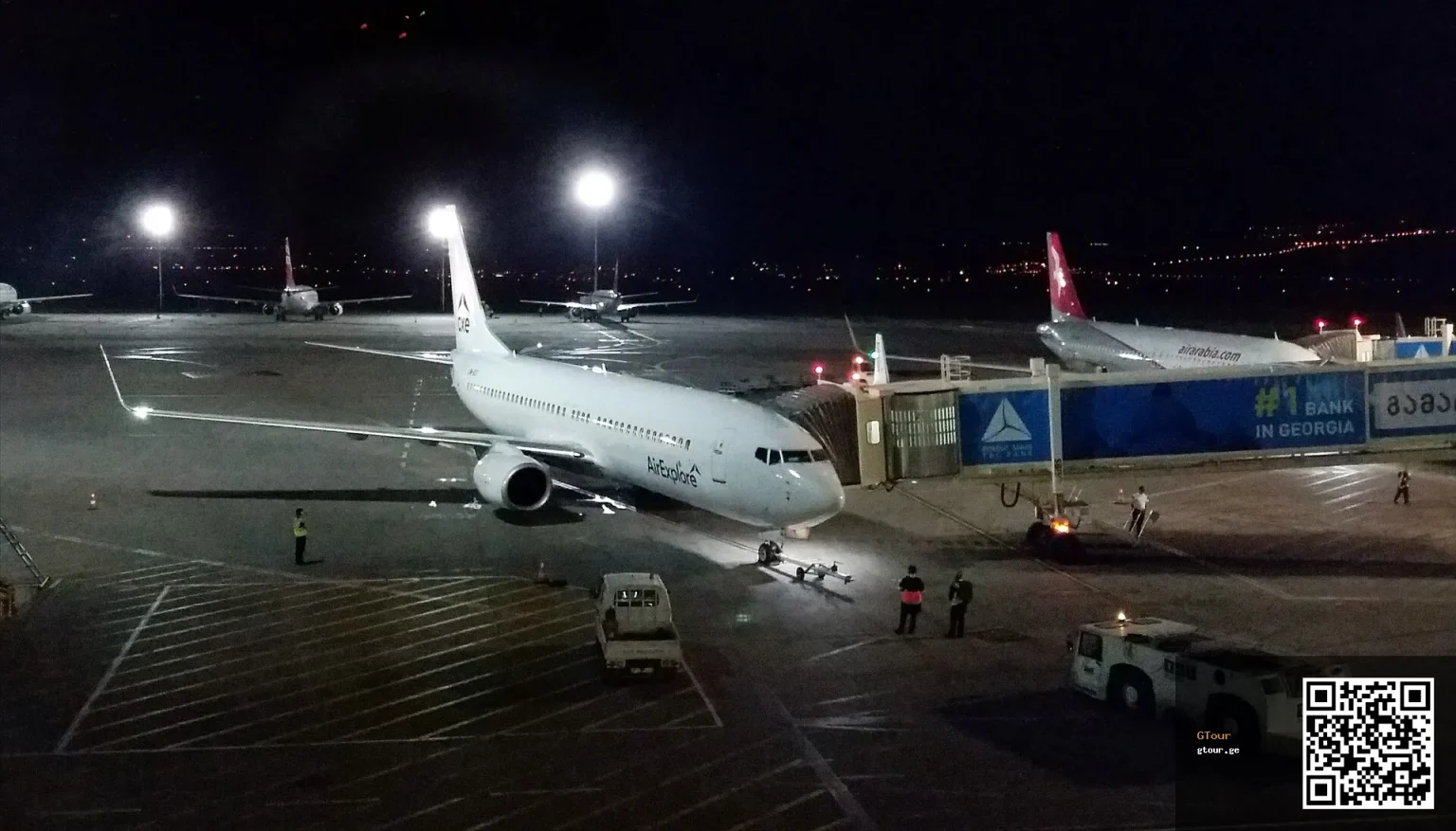 A Vistara jet parked at Tbilisi International Airport's terminal gate at night.