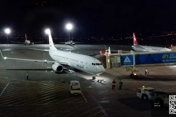 A Vistara jet parked at Tbilisi International Airport's terminal gate at night.