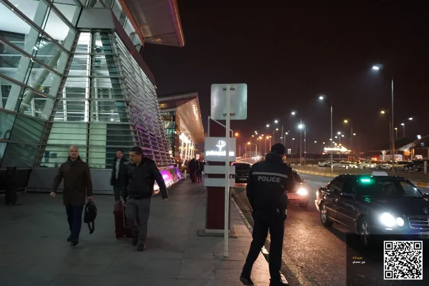 Taxis and arriving passengers outside Tbilisi International Airport at night.