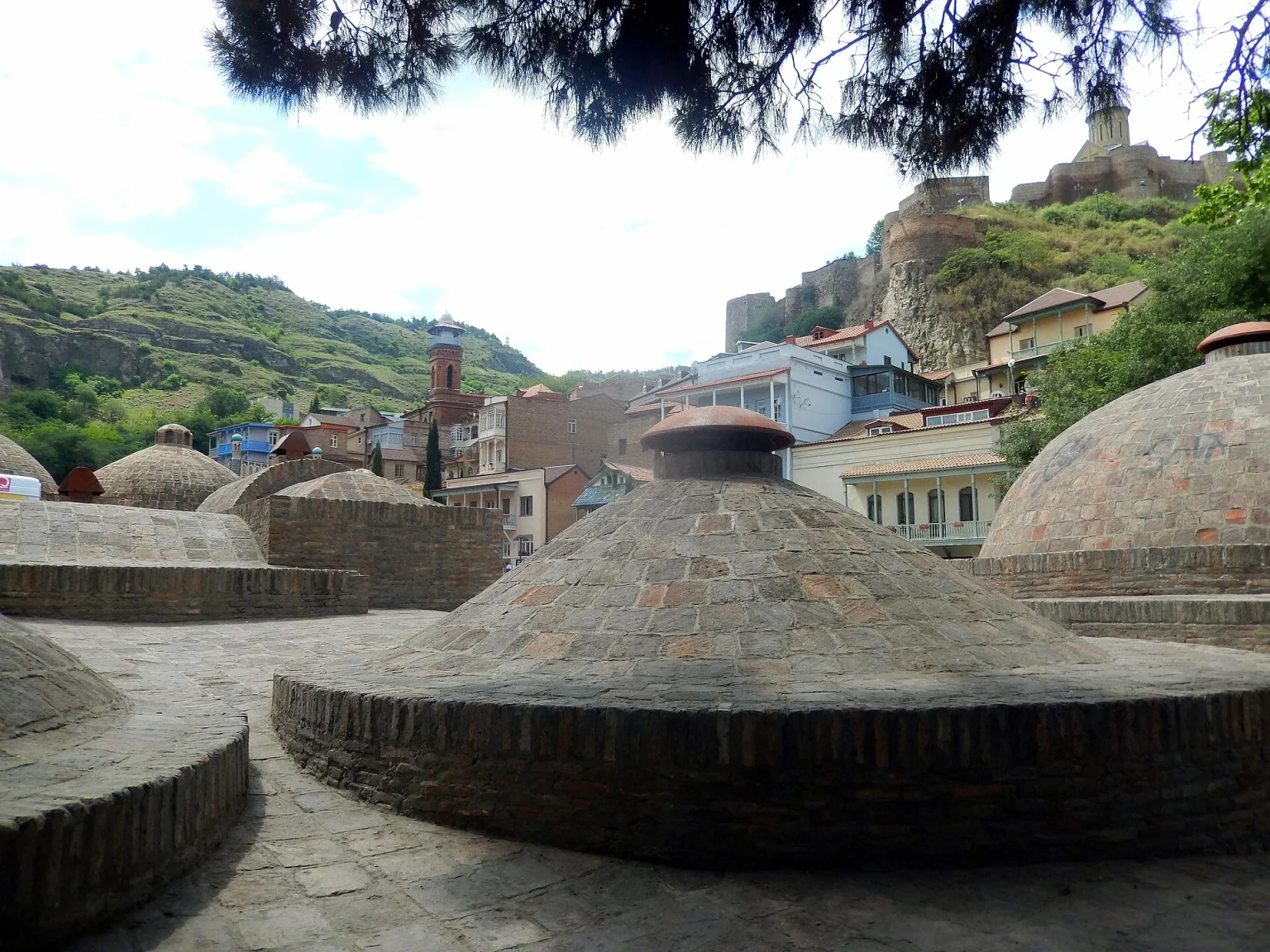Brick domes of Tbilisi's historic sulphur baths rise beneath the Narikala fortress in Abanotubani.