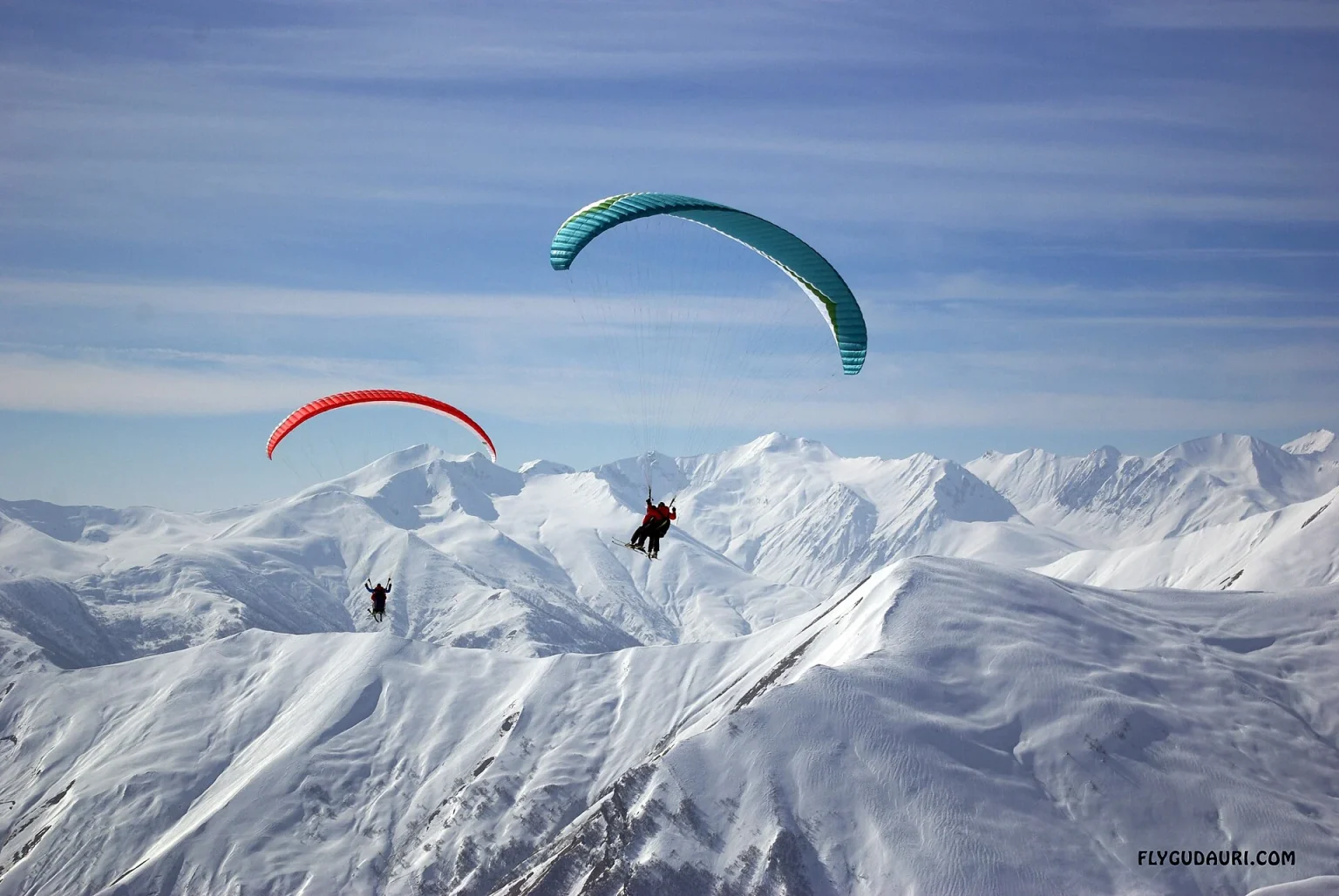 Tandem paragliders soaring over the snowy peaks above Gudauri, Georgia.