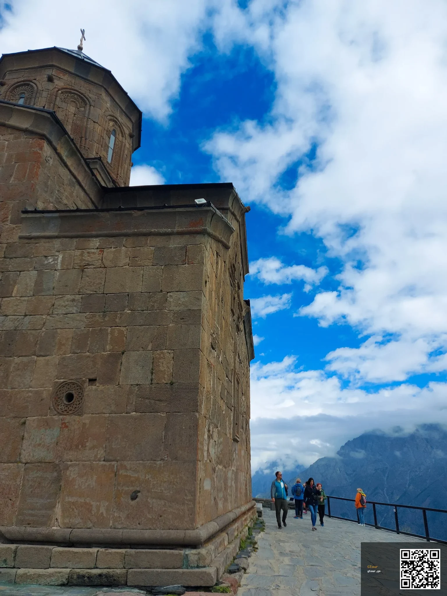 Visitors walk along the stone terrace at Gergeti Trinity Church high above Kazbegi.