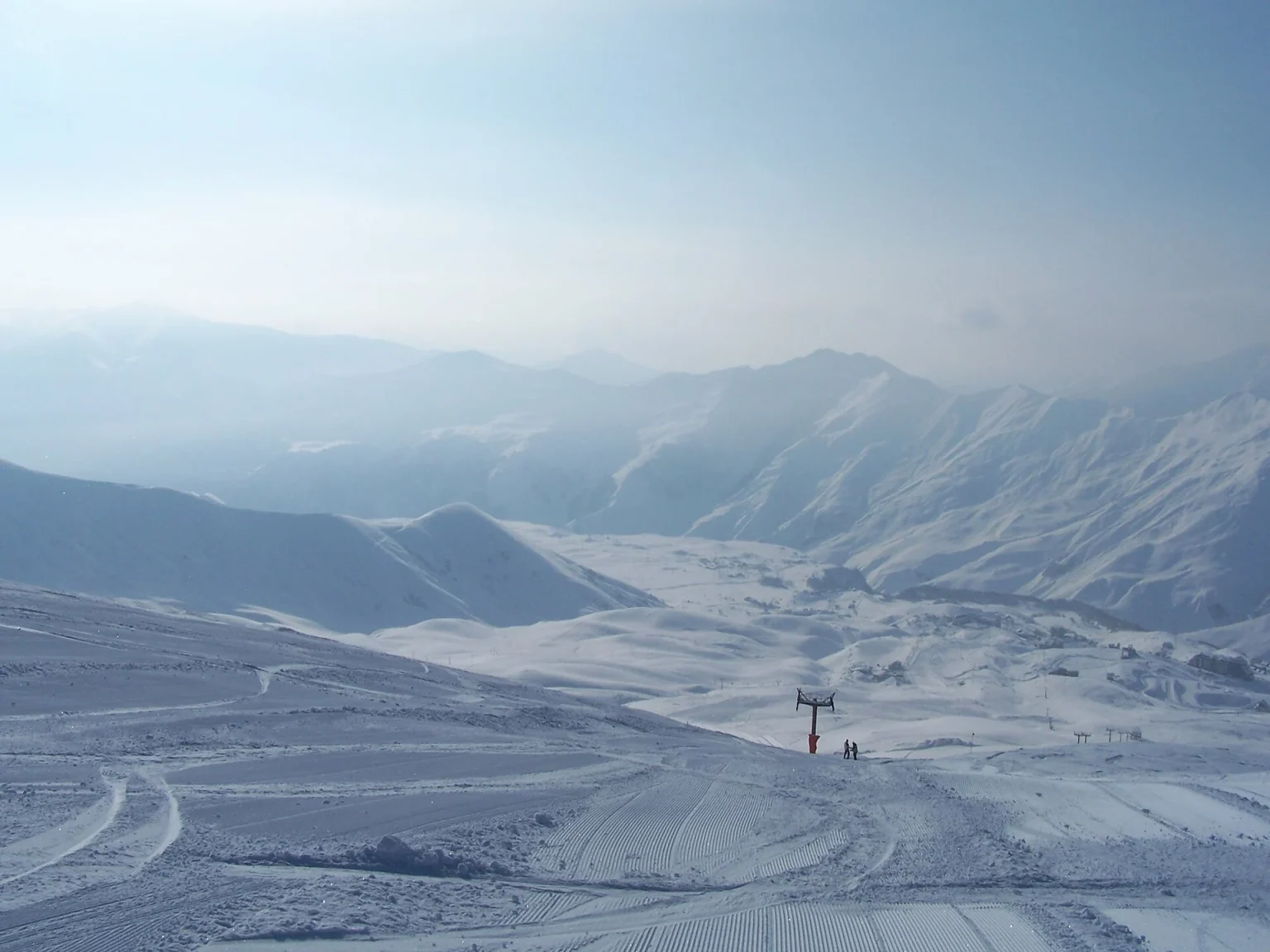 A chairlift and skiers crossing the vast snowy slopes above Gudauri resort.