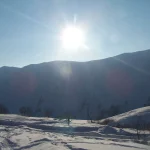 A skier crosses a sunlit snowfield beneath the mountains above Gudauri.