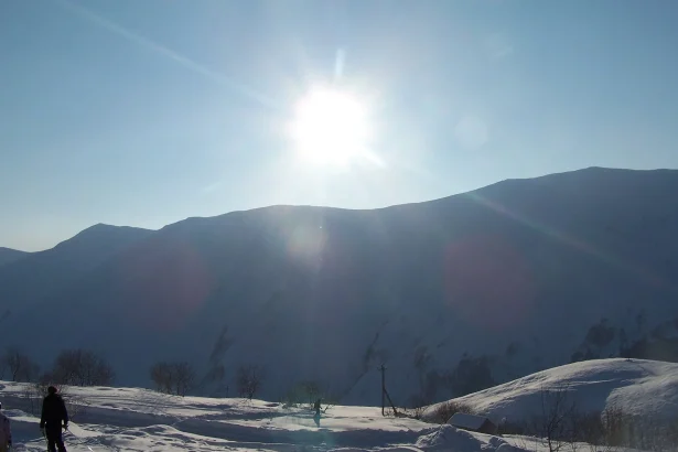 A skier crosses a sunlit snowfield beneath the mountains above Gudauri.