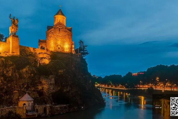 Metekhi Church and the Kartlis Deda statue overlook the Kura River in Tbilisi's old town at dusk.