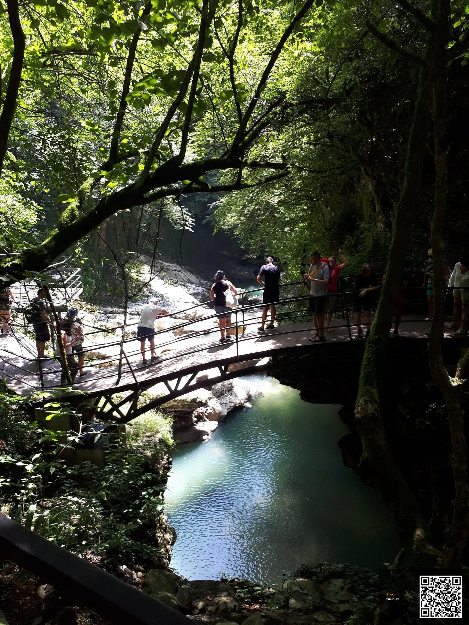 Tourists cross a bridge over the turquoise water of Martvili Canyon, a popular Georgian day trip.