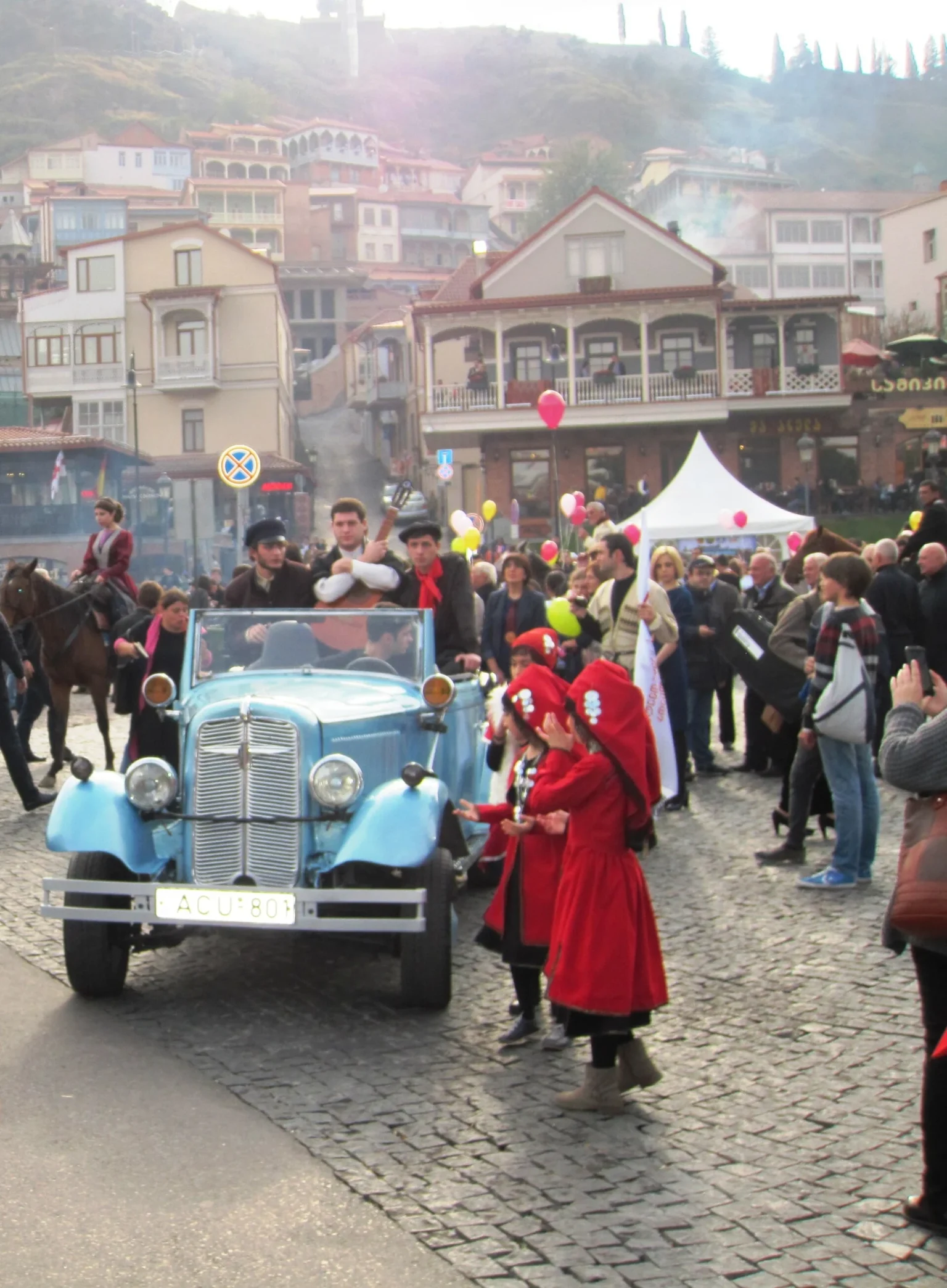 A costumed Tbilisoba parade with a vintage car and horsemen winds through Tbilisi's old town.