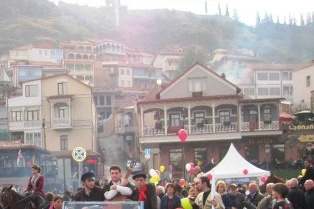 A costumed Tbilisoba parade with a vintage car and horsemen winds through Tbilisi's old town.