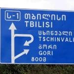 A road sign near Tbilisi shows place names in both Georgian Mkhedruli script and Latin transliteration.