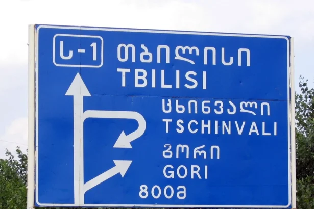 A road sign near Tbilisi shows place names in both Georgian Mkhedruli script and Latin transliteration.